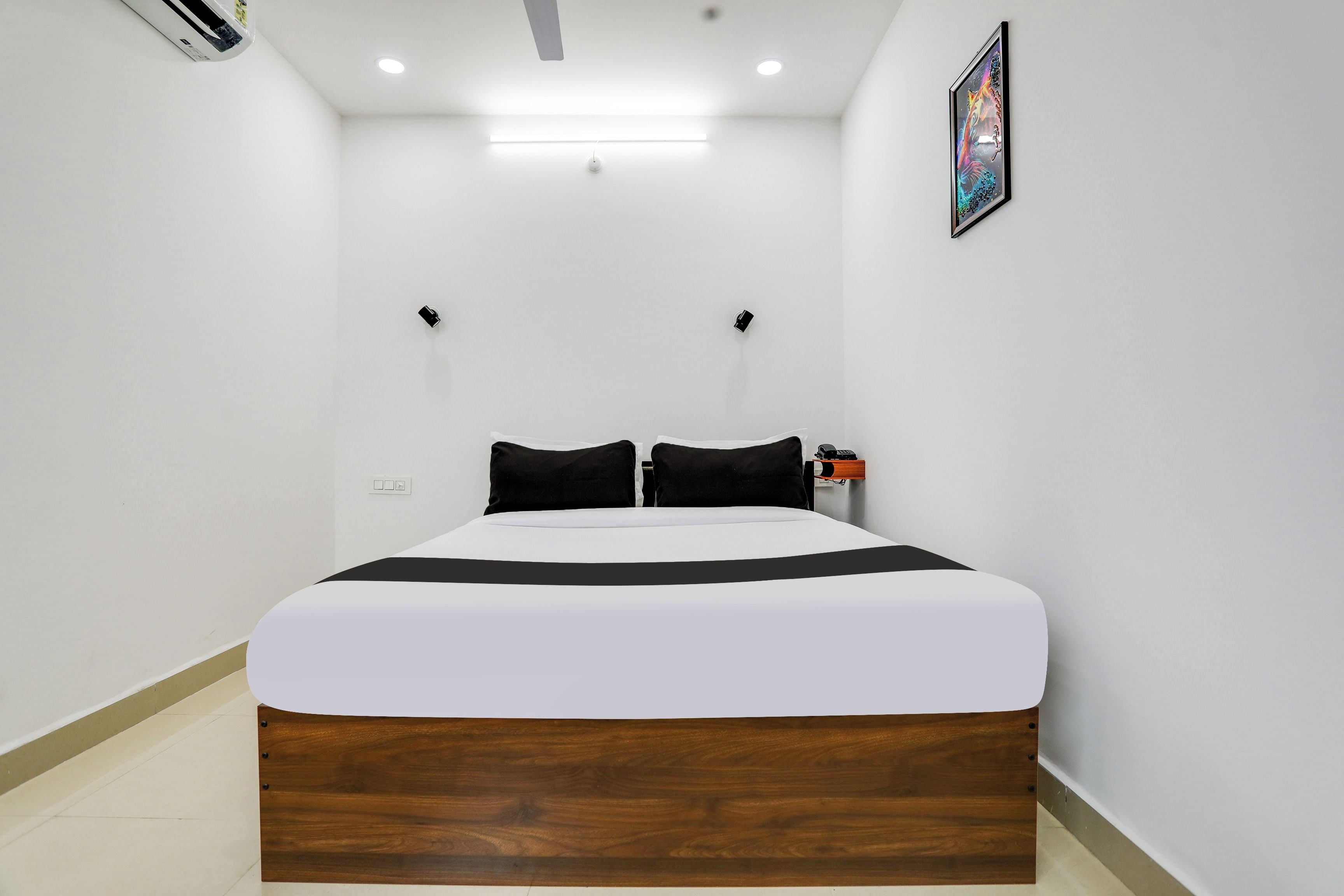 A hotel room with a bed, a bedside table, a wall-mounted light, and a ceiling fan.