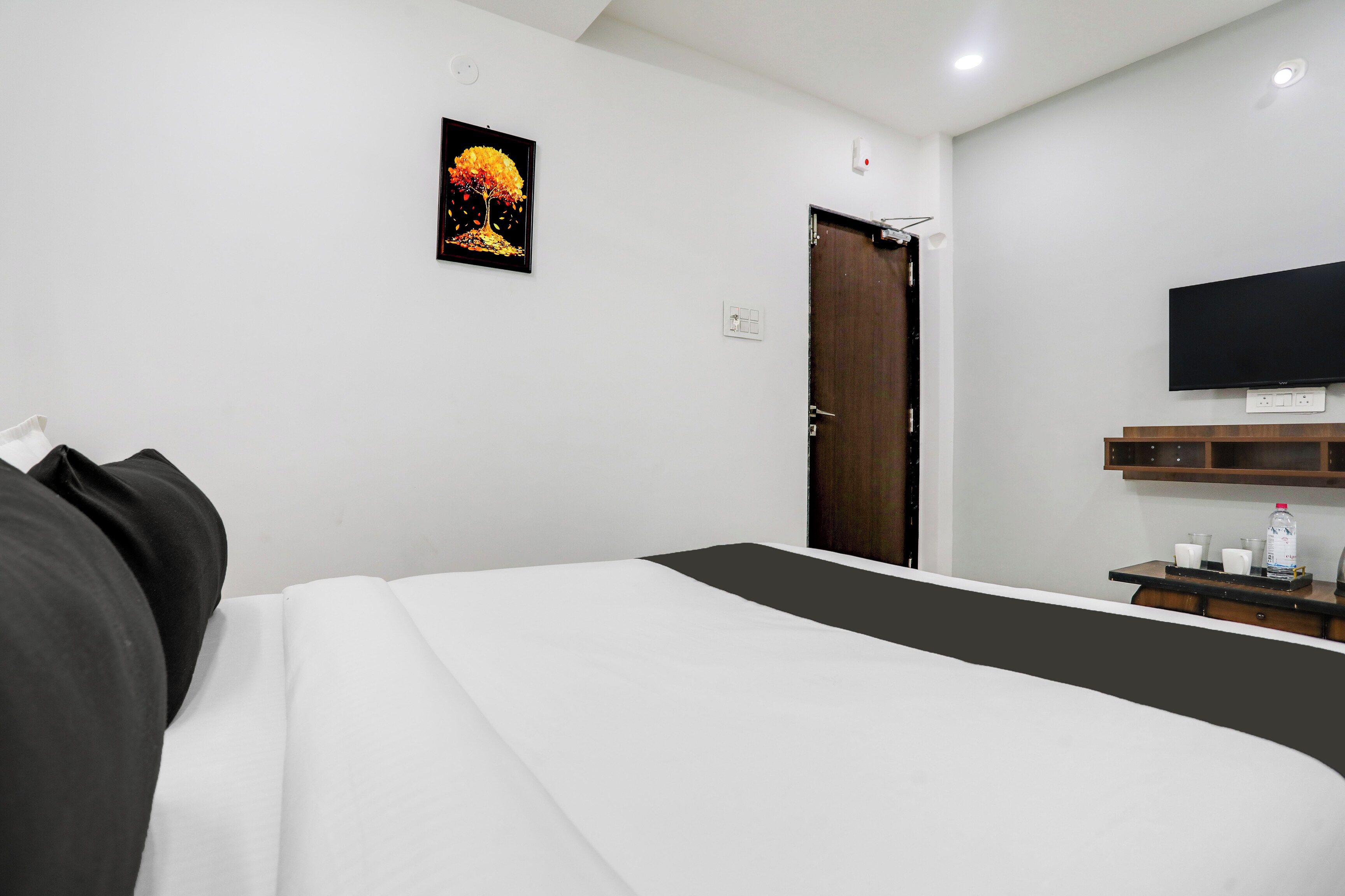 Een hotelkamer met een bed, een aan de muur bevestigde televisie, een deur en een klein tafeltje met een fles en glazen.