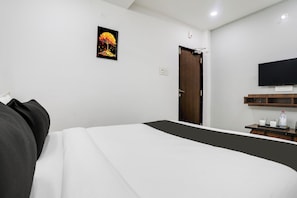 A hotel room with a bed, a TV mounted on the wall, a door, and a small table with a bottle and glasses. - Collection O De Alphabet Hotel (Hyderabad)