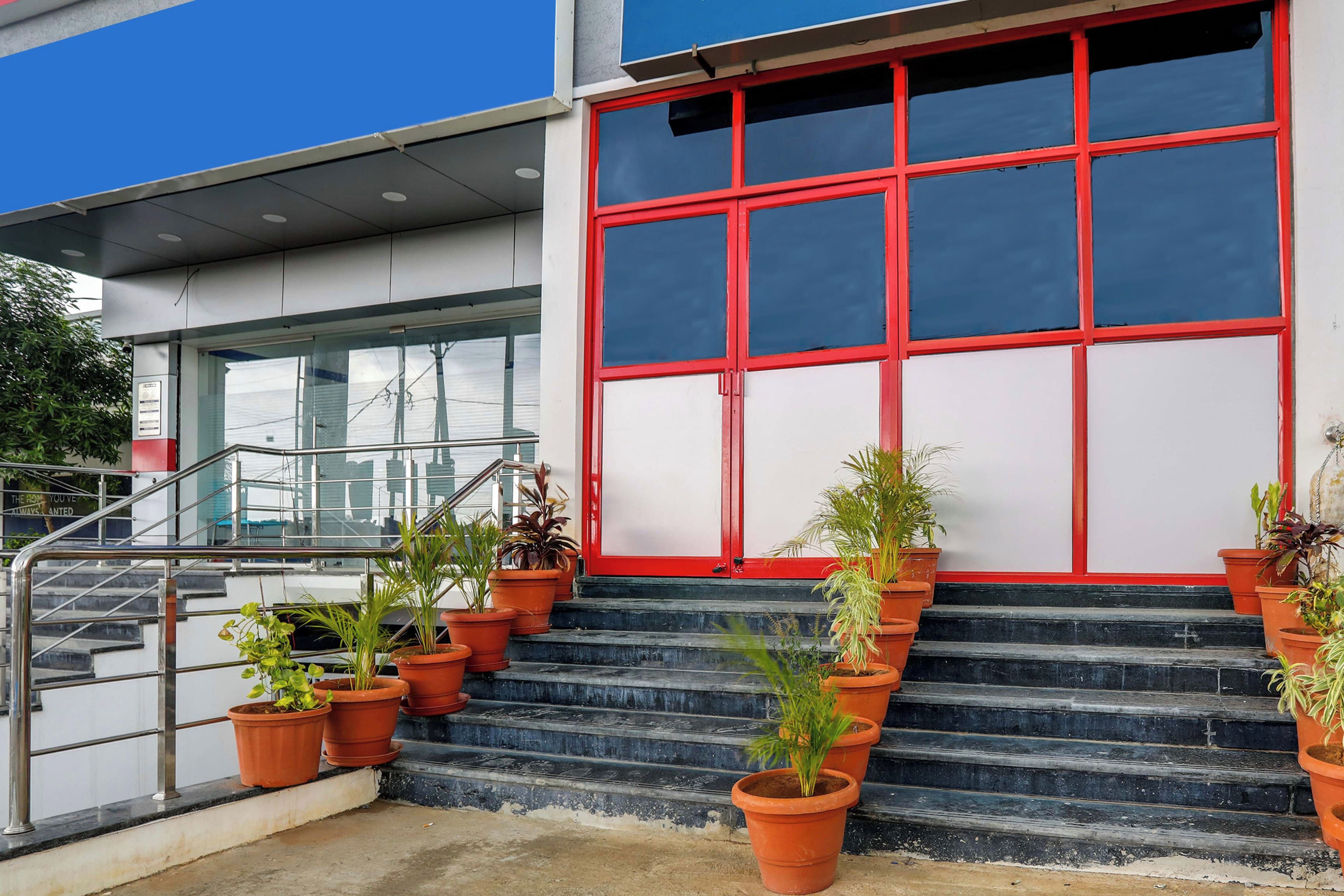 A building with a red-framed entrance, a staircase with potted plants, and a metal railing.