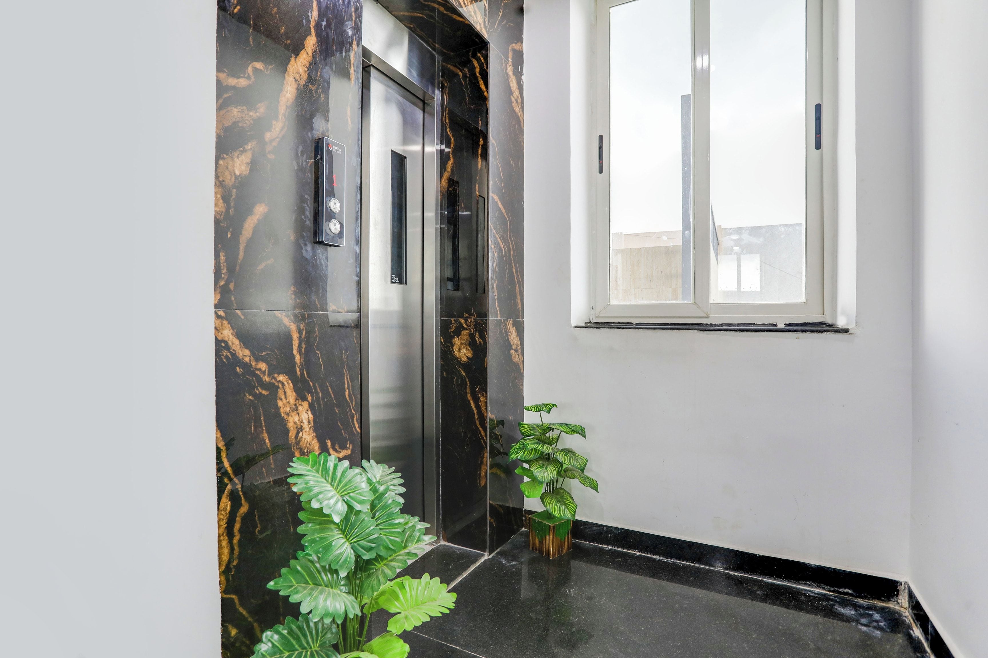 A modern elevator with marble walls and a potted plant beside it.