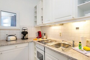 A kitchen with white cabinets, a stainless steel sink, a toaster, a coffee maker, and a window. - Bellevue in the Villa Glückspilz (Binz)