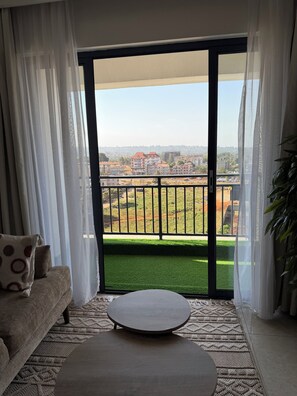 Ein Zimmer mit einer Couch, einem runden Tisch und Blick durch ein großes Fenster mit Balkon.