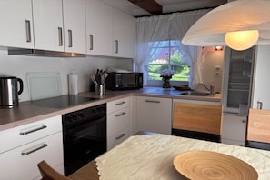 A modern kitchen with white cabinetry, a stainless steel kettle, a microwave, and a wooden table with a bowl. - Holiday apartment with 2 bedrooms (Steinberg)
