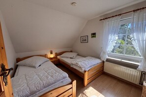 A room with two wooden beds, a radiator, a window with curtains, and a wall-mounted light. - Holiday apartment with 2 bedrooms (Steinberg)
