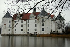 A large white building with multiple towers and a red roof, situated by a calm body of water. - Holiday apartment with 2 bedrooms (Steinberg)