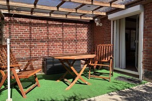 Een terras met een bakstenen muur, een houten tafel en stoelen.