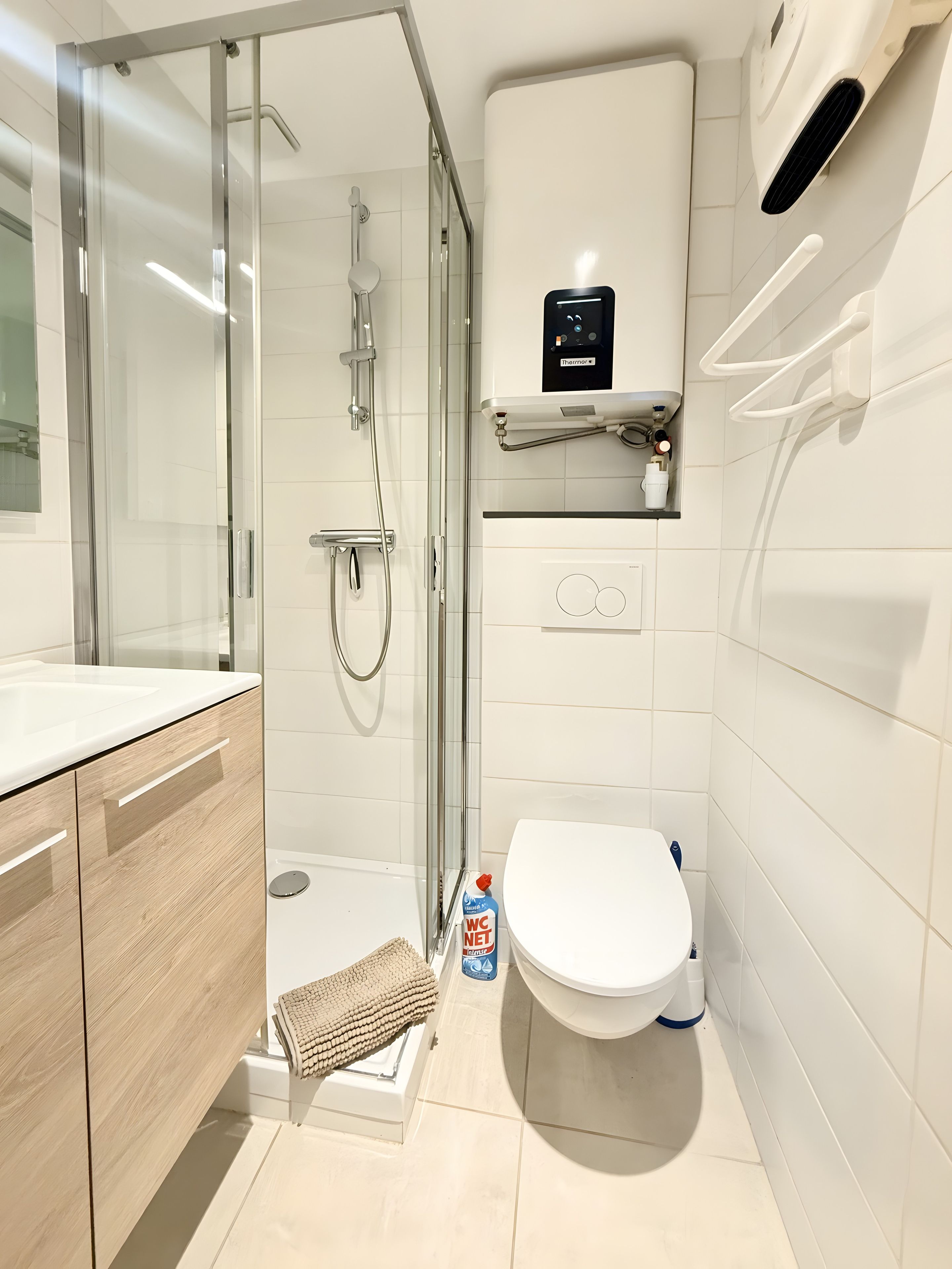 A modern bathroom with a glass-enclosed shower, a white toilet, and a sink with wooden cabinetry.
