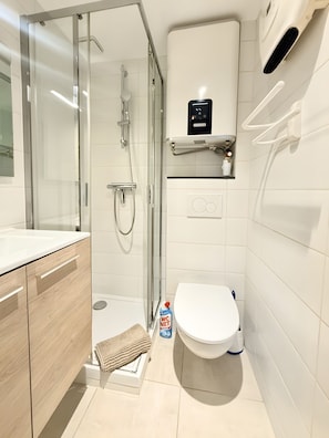 A modern bathroom with a glass-enclosed shower, a white toilet, and a sink with wooden cabinetry. - Studio 'Lumière Alpine' in the Hyper Center (Villard-de-Lans)