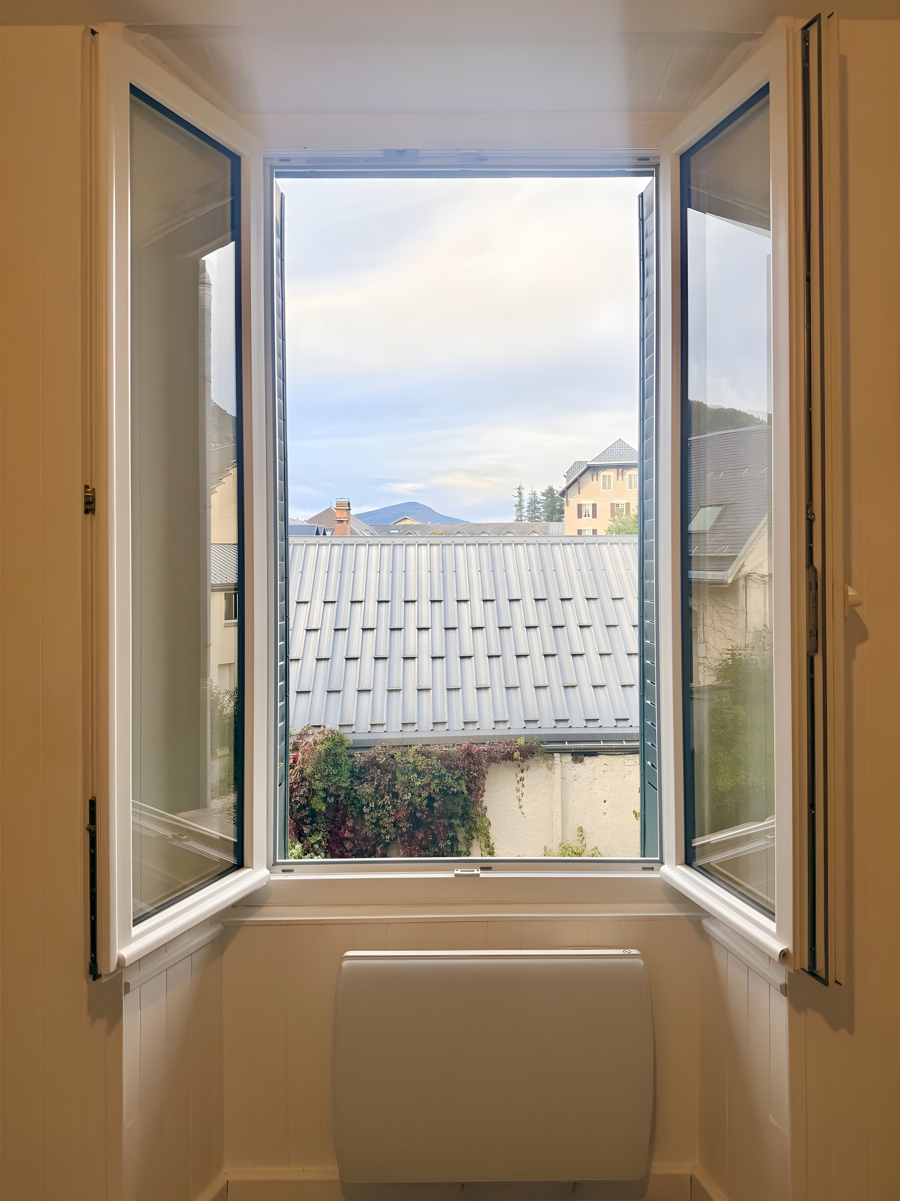 Une pièce avec une fenêtre donnant sur un quartier résidentiel, un radiateur et une porte.