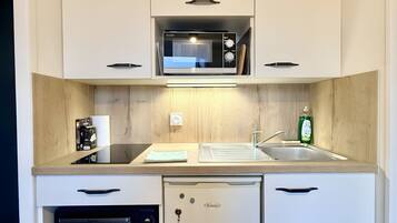 A compact kitchen with a microwave, oven, and refrigerator, featuring white cabinetry and a wooden countertop.