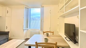A modern, minimalist living space with a dining area, a television, and a view of the sky.