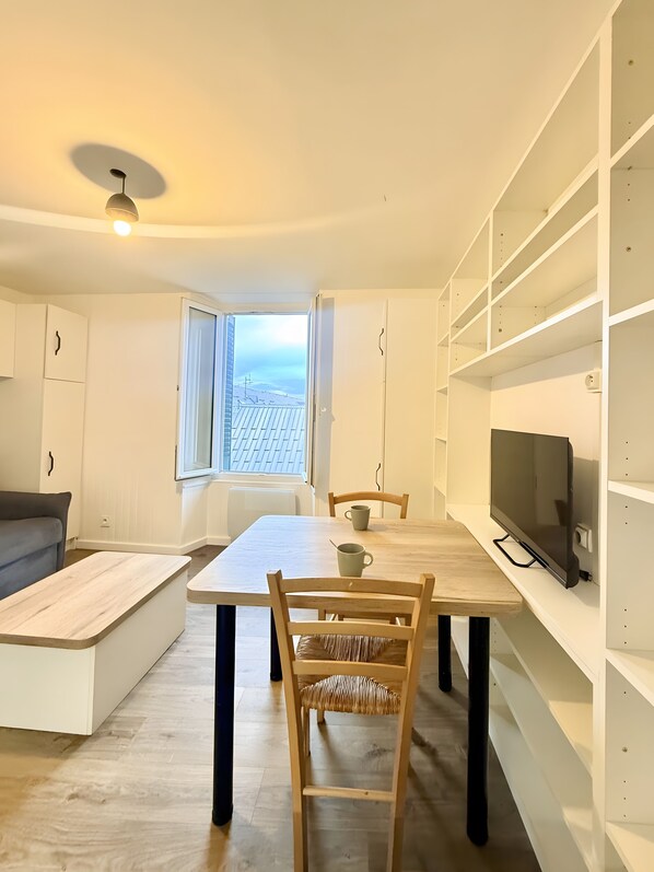 A modern, minimalist living space with a dining area, a television, and a view of the sky. - Studio 'Lumière Alpine' in the Hyper Center (Villard-de-Lans)