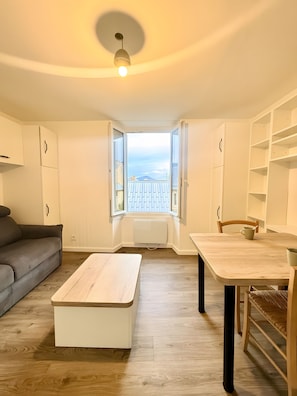 Un espacio habitable compacto con un sofá, una mesa de comedor y vistas a través de una ventana abierta.