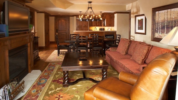 A living room with a fireplace, a television, a sofa, and a dining area with chairs and a chandelier.