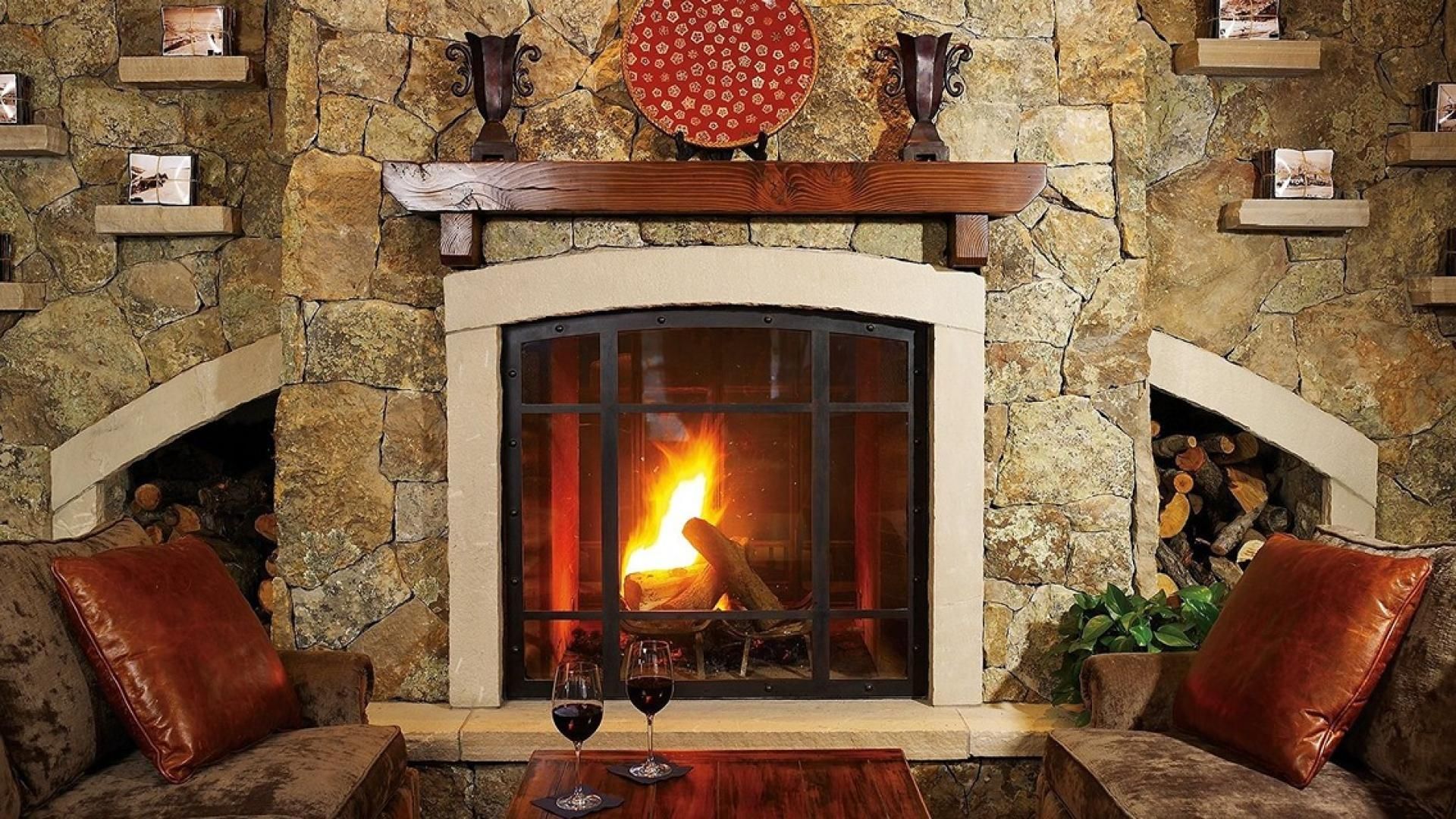 A stone fireplace with a fire, flanked by leather sofas and a table with a wine glass.