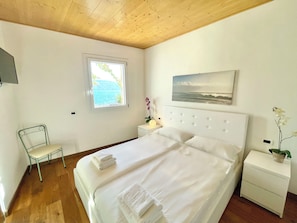 A bedroom with a bed, a chair, a nightstand, a window, and a wall-mounted picture. - D1MORA Nautilus - incredible lakeside location (Lombardia)