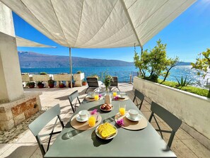Ein Essbereich im Freien mit einem Tisch, der für ein Frühstück gedeckt ist, mit Blick auf eine malerische Landschaft aus Meer und Bergen.
