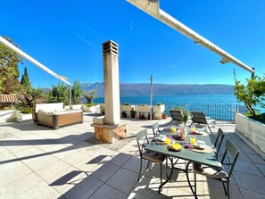 Eine Terrass mit Tisch, gedeckt für ein Frühstück, mit Blick auf ein Gewässer und Berge.