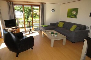 Sala de estar com sofá, mesa de centro, televisão e porta de vidro deslizante para um jardim.