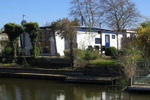 Ein Haus mit einer blauen Tür, umgeben von viel Grün und einem Gewässer.