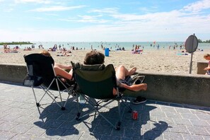 Ein Strand mit Menschen, die am Sand liegen und in Stühlen entspannen, ein klarer Himmel und ein ruhiges Meer.