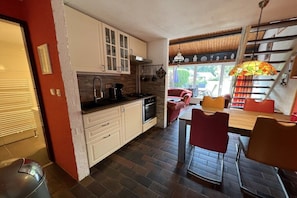 A compact kitchen with modern appliances, a dining area with red chairs, and a staircase with a stained glass lamp. - Holiday home with 1 bedroom (Bruinisse)