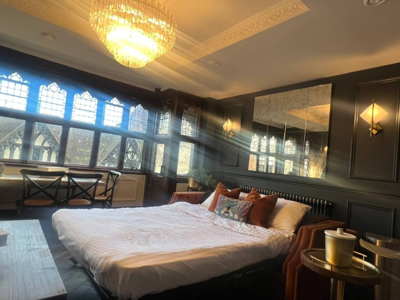 Un dormitorio con una cama grande, un escritorio y una silla. Hay ventanas con vistas a edificios.