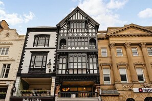 Una hilera de edificios con estilos arquitectónicos diversos, incluyendo una casa de estilo Tudor con fachada blanco y negra y un edificio clásico con columnas.