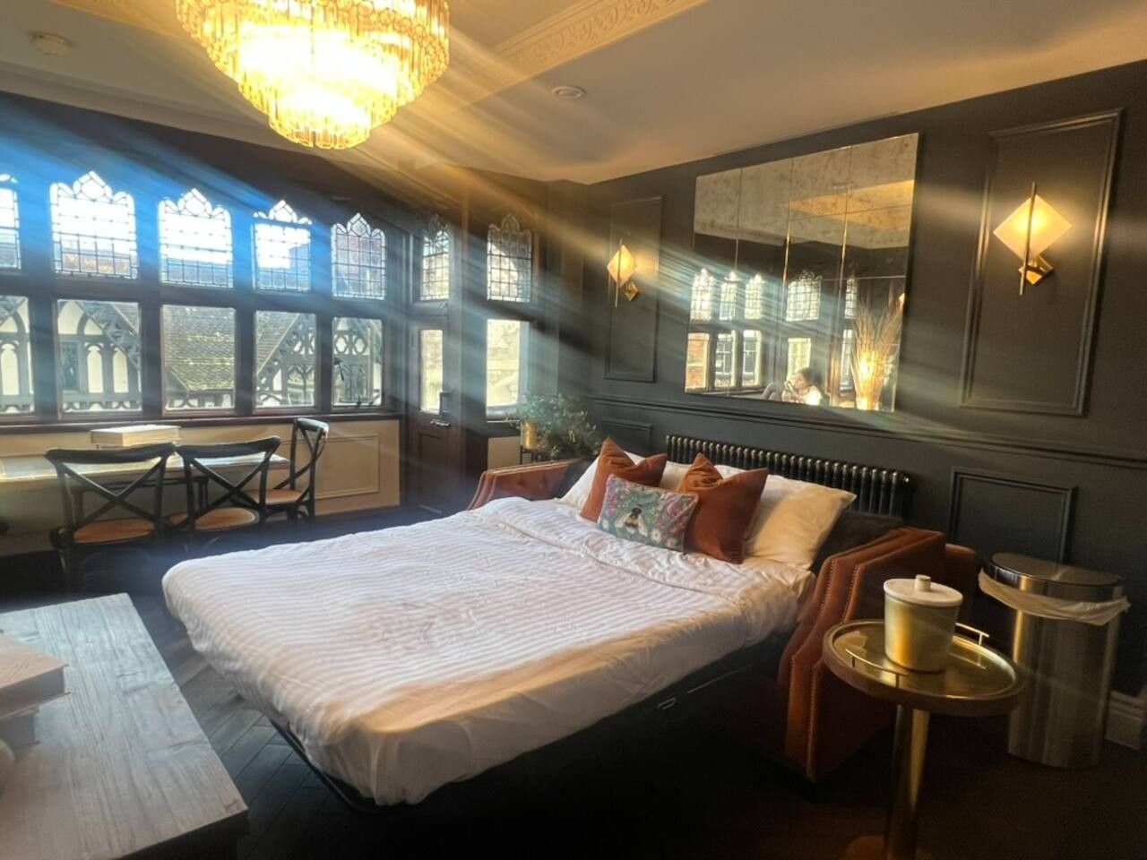 A hotel room with a large bed, a desk, and a chair. There are windows with a view of a building.