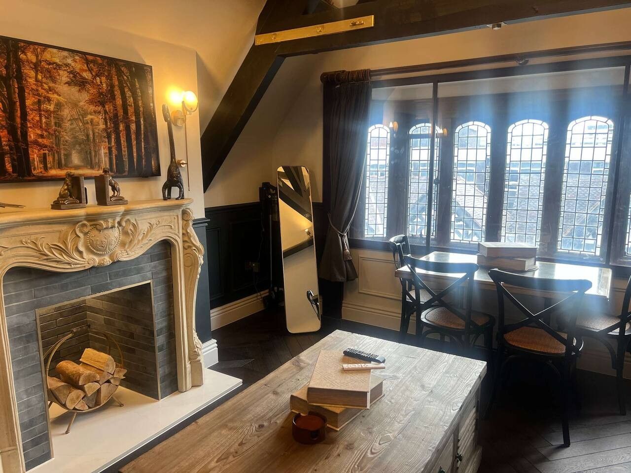 A cozy room with a fireplace, a dining table with chairs, and a large window with curtains.