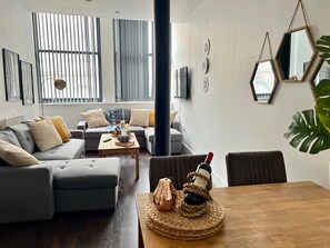 A modern living room with a sofa, coffee table, and a dining table with a bottle and decorative item. - Mathew Street - City 1 BDR apt sleeps 6 (Merseyside)