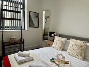 A hotel room with a bed, a bedside table, a mirror, a window with blinds, and a view of the outside. - Mathew Street - City 1 BDR apt sleeps 6 (Merseyside)