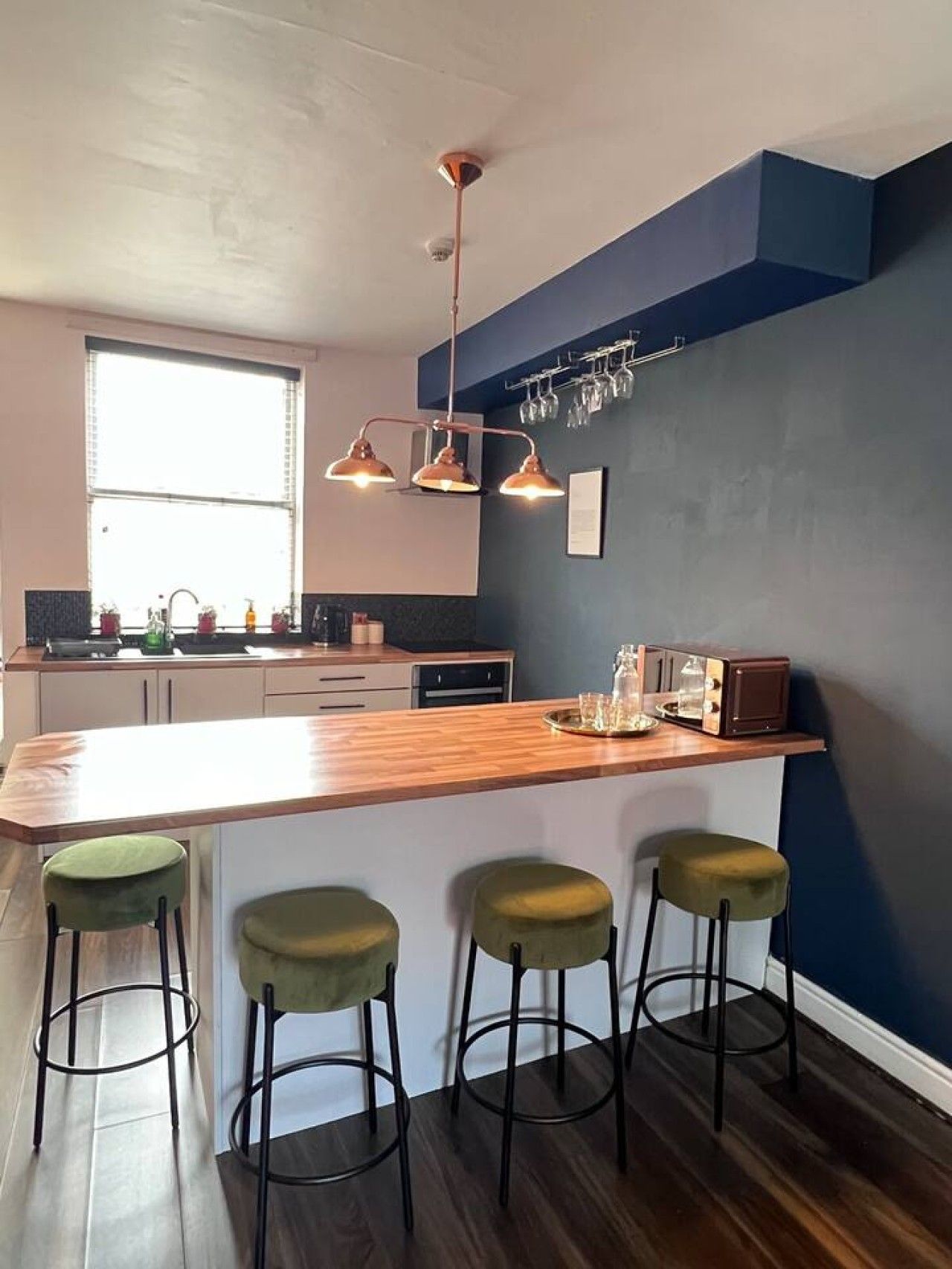 A modern kitchen with a wooden island, bar stools, and a built-in oven.