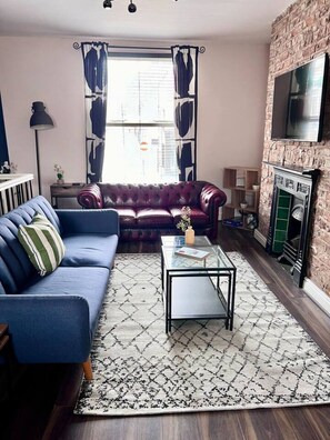A living room with a blue sofa, a red leather couch, a glass coffee table, and a patterned rug. - Stylish and Central - 2 bed, sleeps 4 (Merseyside)