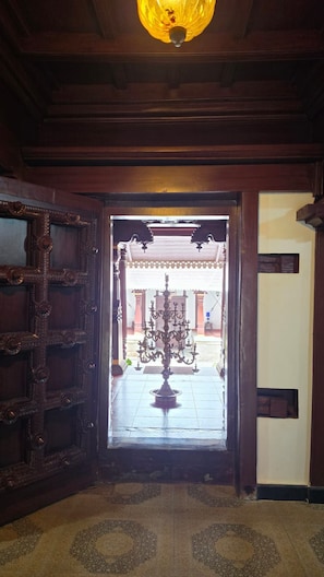 A wooden door with intricate carvings leading to a courtyard with a decorative iron gate and a central pillar.