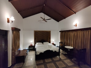 A hotel room with a bed, a desk, a chair, a ceiling fan, and two wall-mounted lamps. - Aralaguppe Heritage Homestay (Chikkamagaluru)