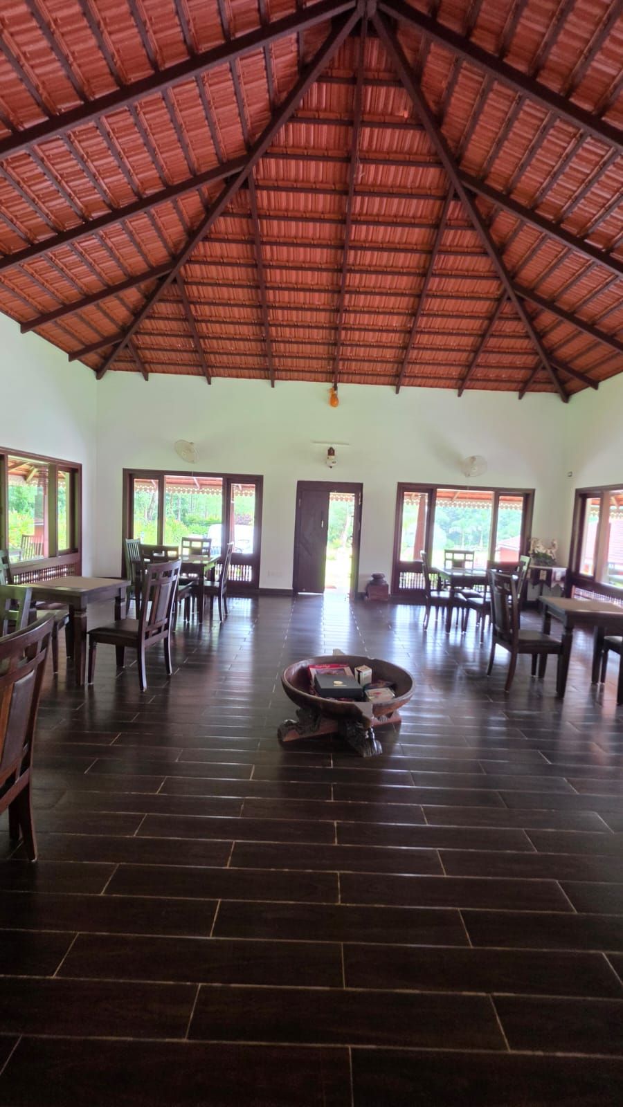 A spacious indoor area with a high, sloped roof and a tiled floor. There are multiple tables and chairs arranged for dining.
