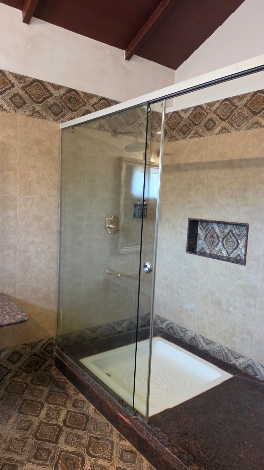 A glass-enclosed shower with a tiled floor and a patterned wall.