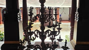 Un candelabro de bronce tradicional en un espacio interior bien iluminado, con suelo de baldosas y elementos arquitectónicos de madera.