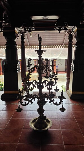 Un candelabro de bronce tradicional en un espacio interior bien iluminado, con suelo de baldosas y elementos arquitectónicos de madera.