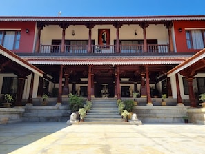 A two-story building with a traditional architectural style, featuring a balcony with ornate railings and a central entrance with steps leading up to it.