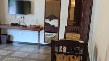 Una habitación con un banco de madera, un televisor fijado en la pared, una cama con cabecero y un espejo.