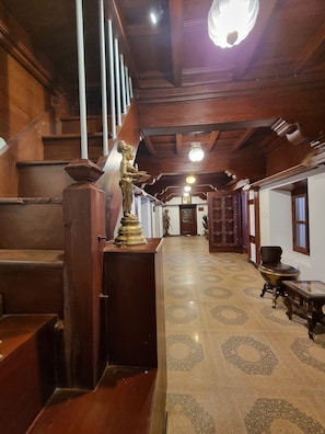A hallway with a wooden staircase, a statue, and a patterned carpet. - Aralaguppe Heritage Homestay (Chikkamagaluru)