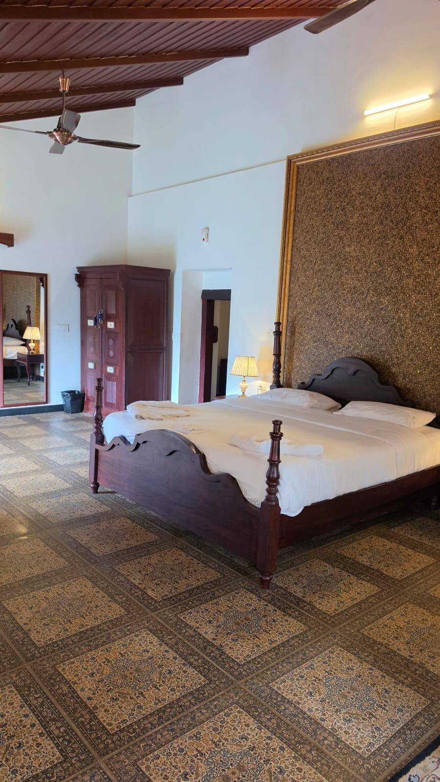 A bedroom with a large bed, a ceiling fan, a wardrobe, and a patterned carpet.