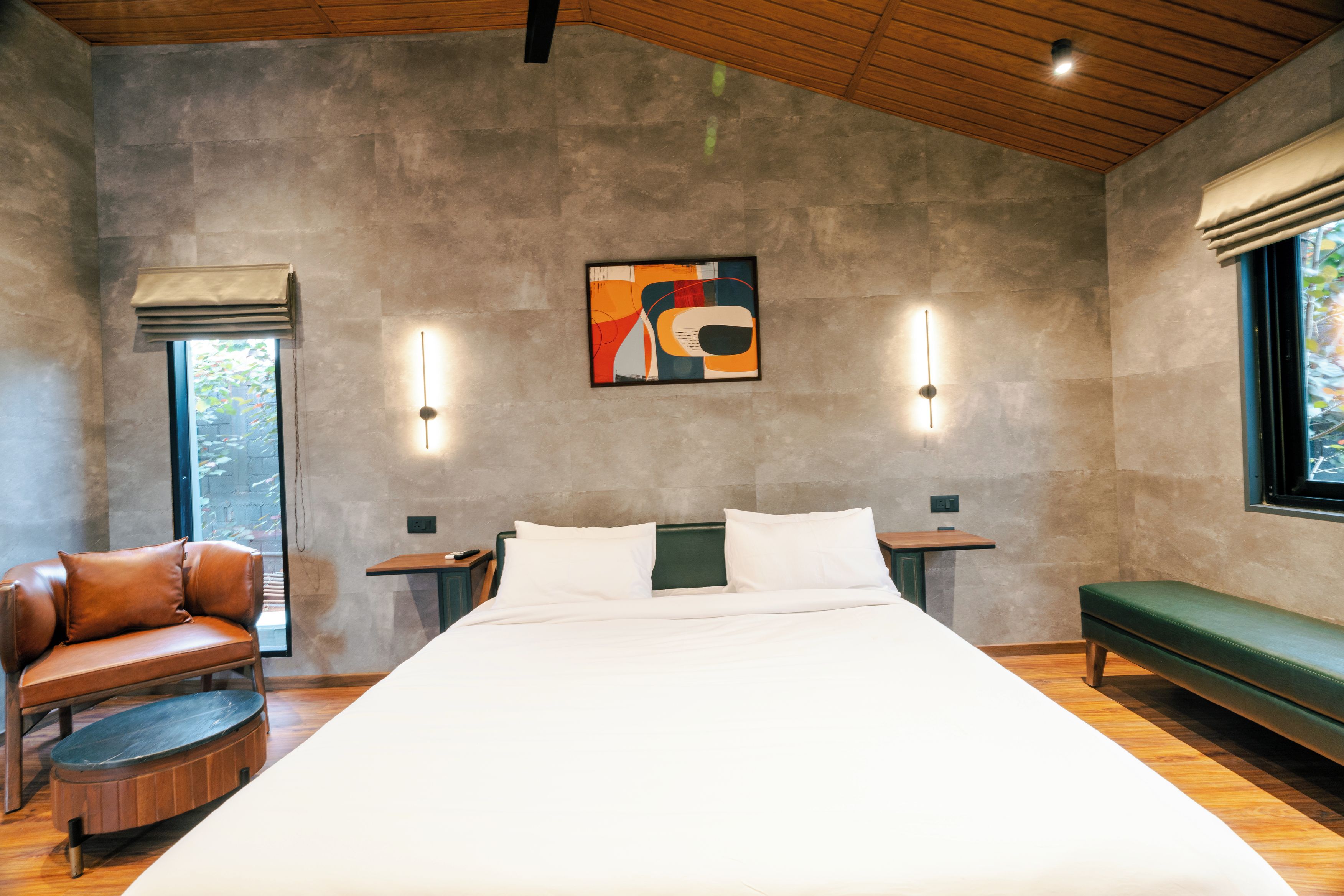 Un dormitorio moderno con una cama grande, un banco verde, una butaca de cuero y una obra de arte colgada en la pared.