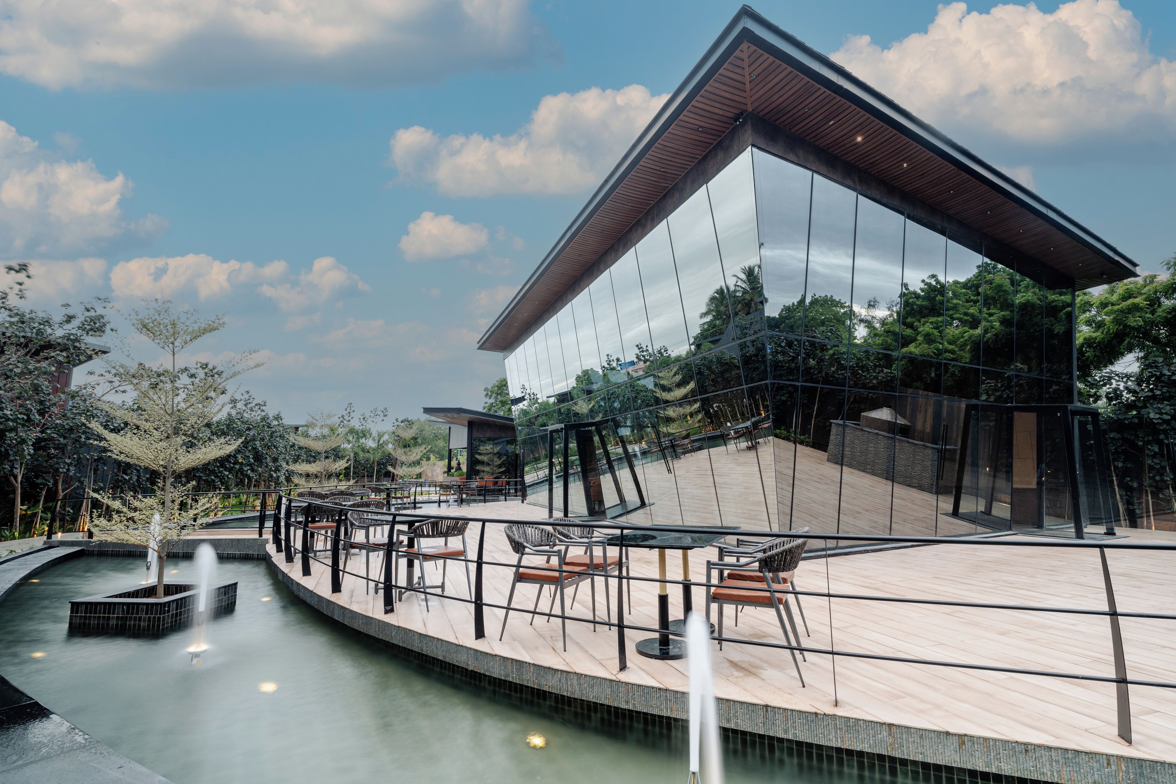 Un bâtiment moderne doté d’une façade en verre réfléchissant, d’une piscine et d’un espace extérieur aménagé pour s’asseoir.