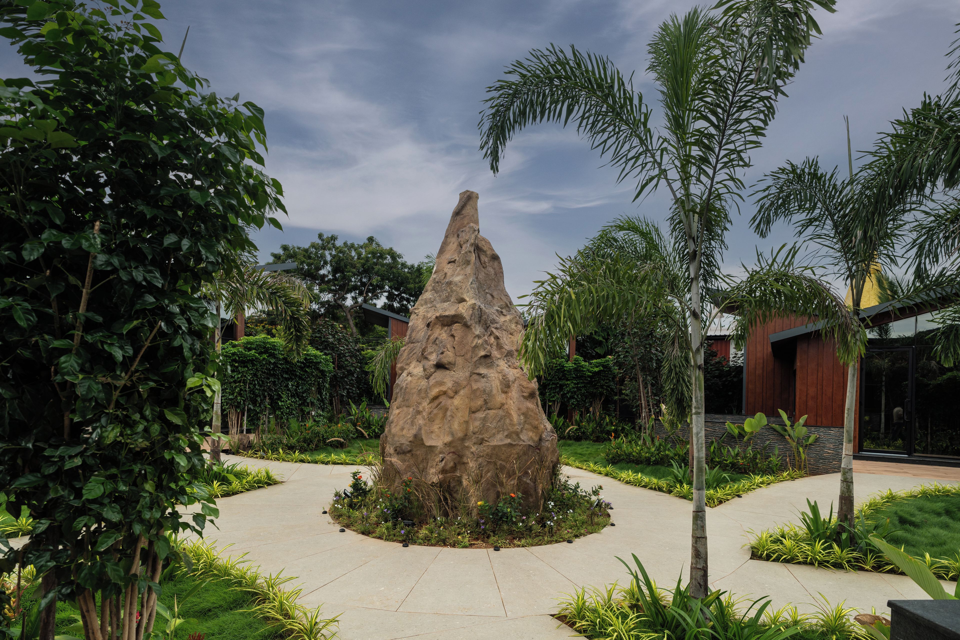 A landscaped garden with a central rock feature, surrounded by various plants and a paved walkway.