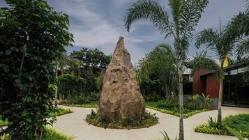 A landscaped garden with a central rock feature, surrounded by various plants and a paved walkway.
