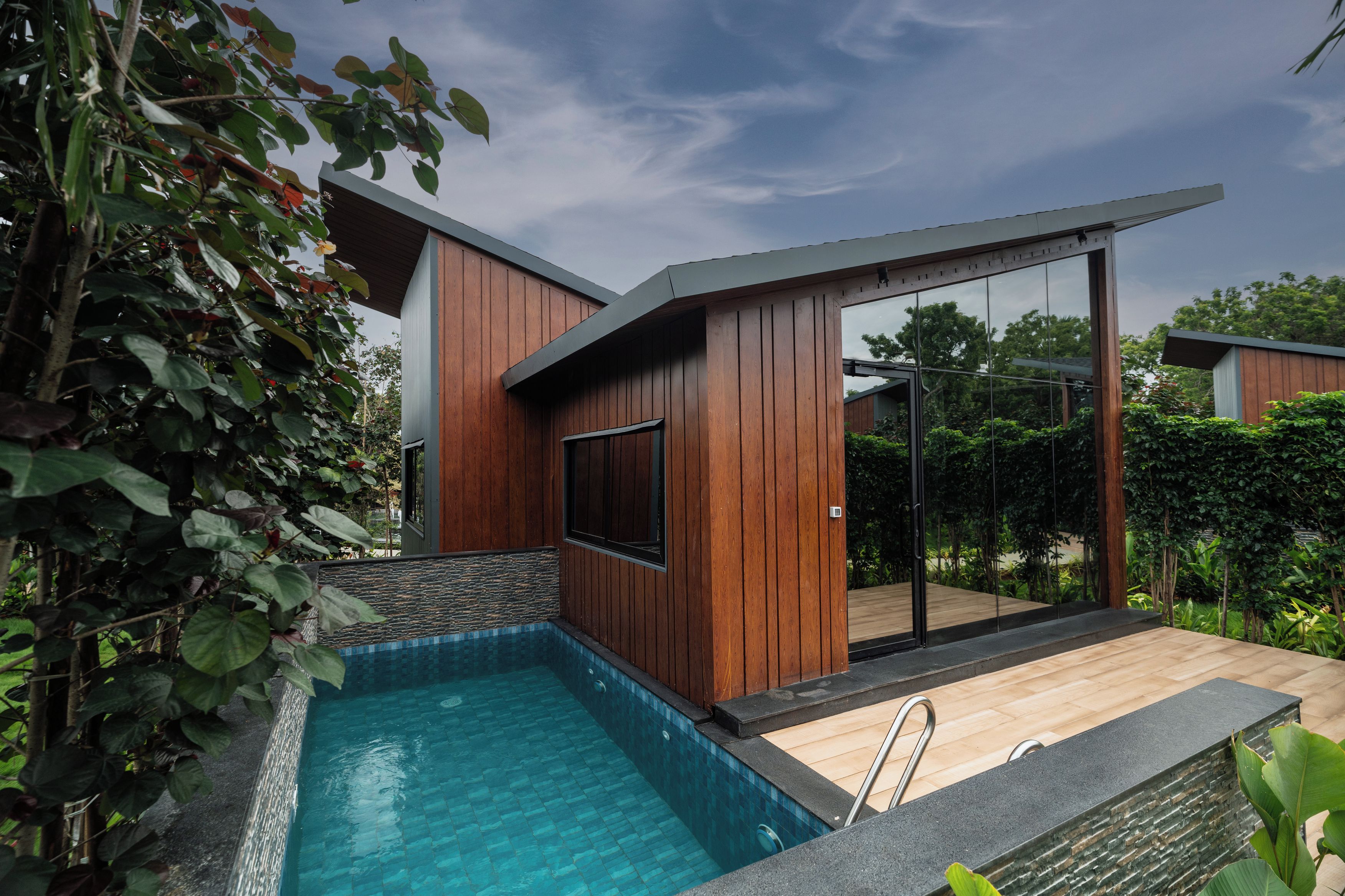 A modern outdoor pool area with a wooden deck and a glass-enclosed patio.